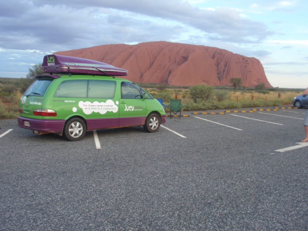 Green rental car and Ayer's Rock during the road trip in the middle of the desert in Australia. Rescued in the middle of the desert