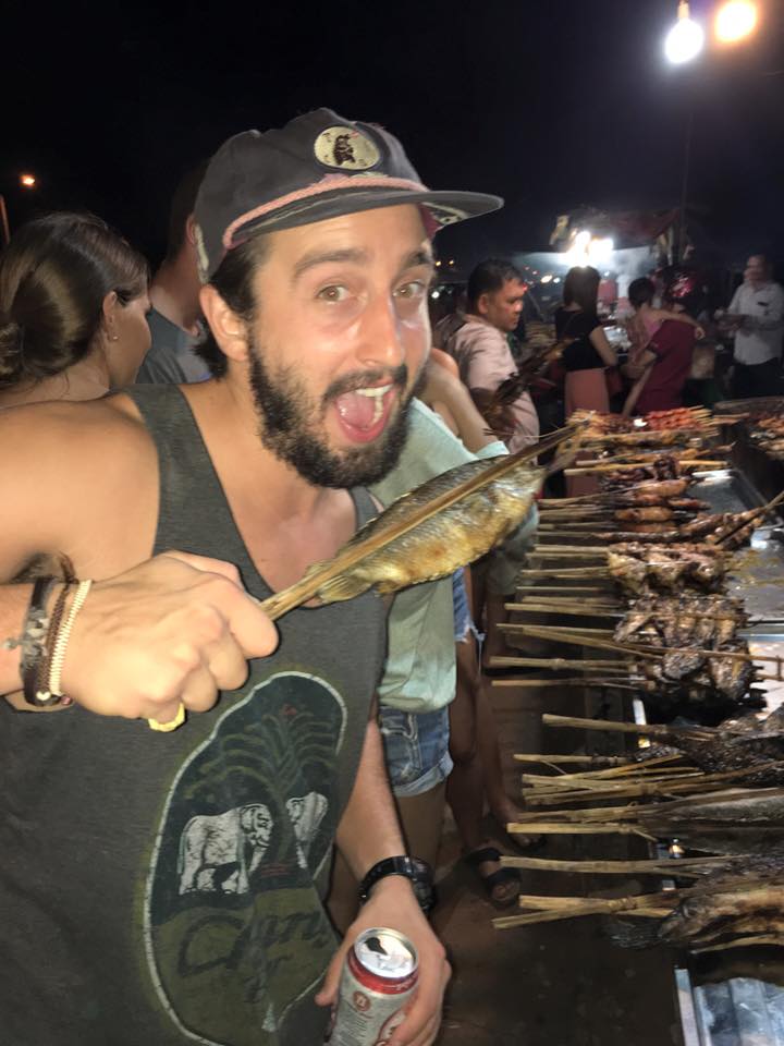 Guy biting on a cooked fish in Cambodia. The craziest food tour in Cambodia