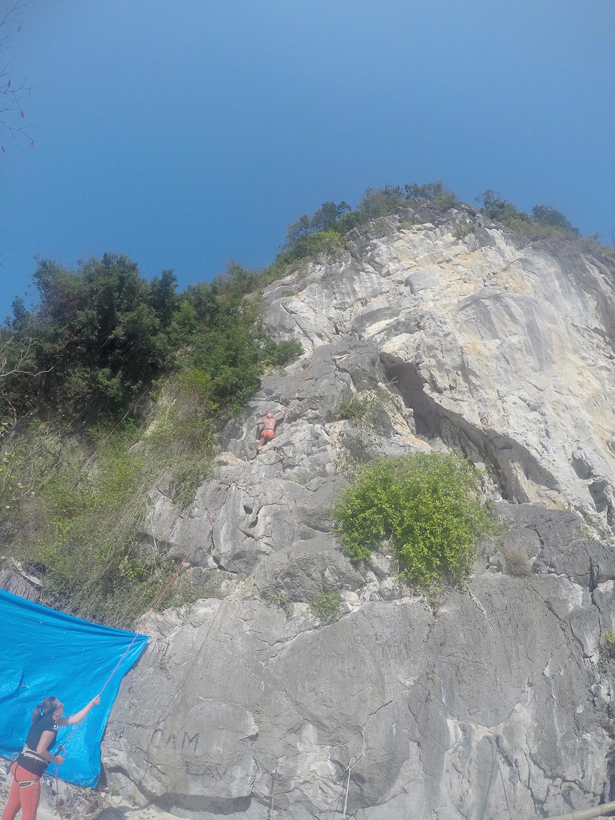 David Simpson climbing the limestone cliffs while a woman watches below in Ha Long Bay, Vietnam. Rock climbing in Ha Long Bay