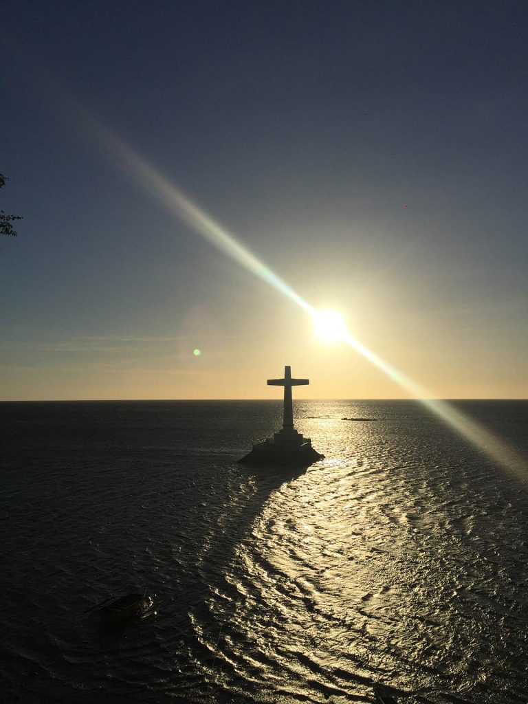 Cross of the Sunken Cemetery at sunset in Camiguin, Philippines. White Island on Camiguin