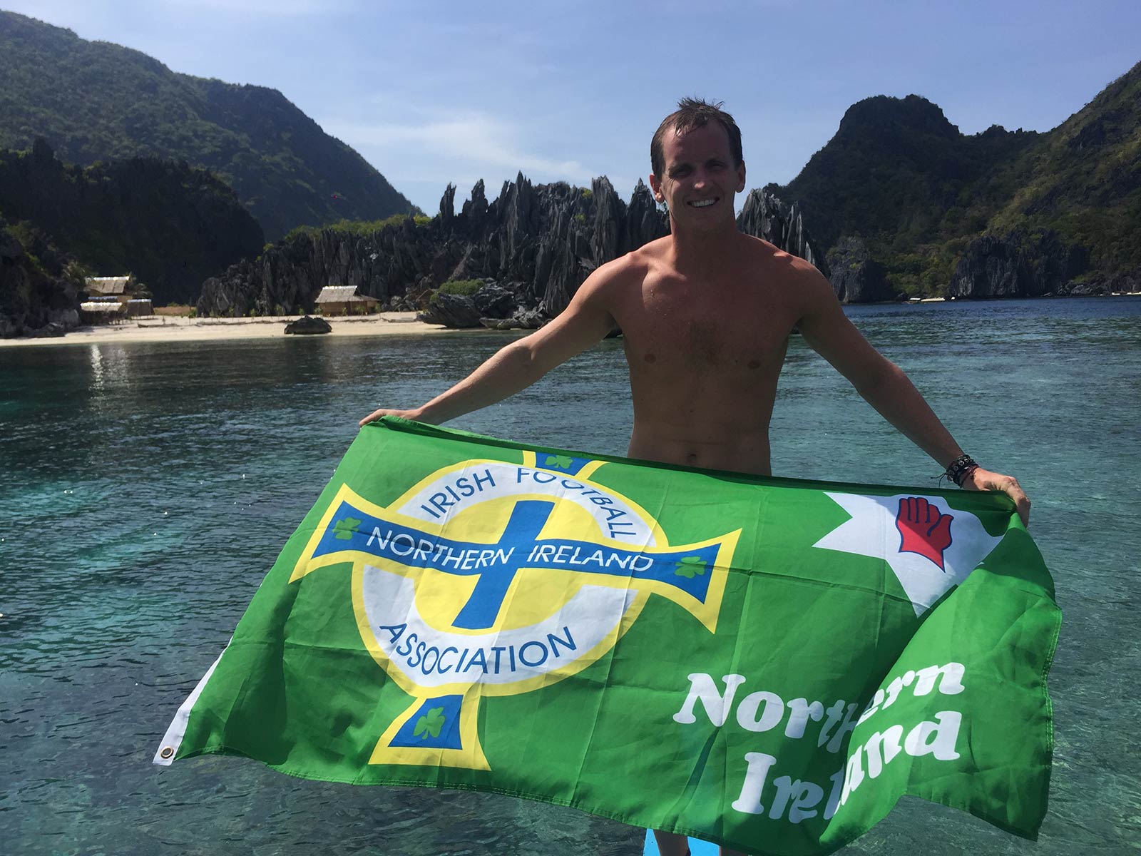 David Simpson holding NI flag at a beach in Nacpan, Philippines. The best beach in the world all to myself