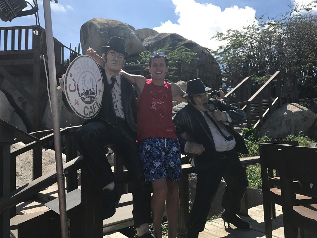 David Simpson standing with two statues in Aruba. Panama Canal & the last of Central America