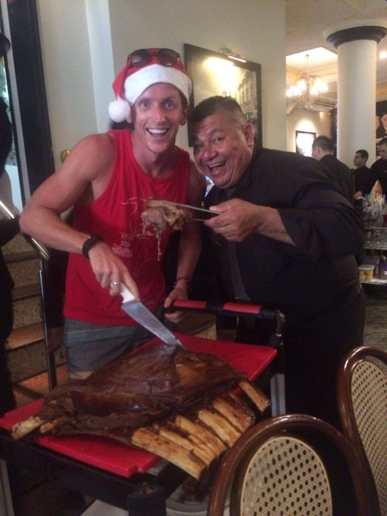David Simpson and local slicing roasted ribs for Christmas lunch in Rio de Janeiro, Brazil. Friends, steak & Copacabana, a perfect Christmas in Rio