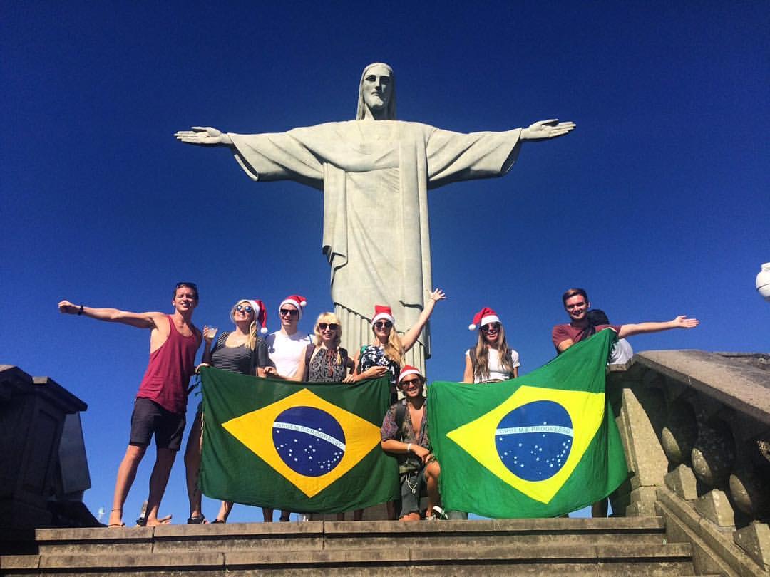 David Simpson and friends holding Brazil flag at Christ the Redeemer statue in Rio de Janeiro, Brazil. Friends, steak & Copacabana, a perfect Christmas in Rio
