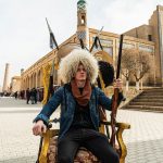 David Simpson wearing a fur hat and seated in the middle of the street in Khiva, Uzbekistan. Crossing in Uzbekistan and the train to Bukhara