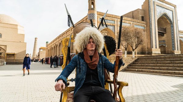 David Simpson wearing a fur hat and seated in the middle of the street in Khiva, Uzbekistan. Crossing in Uzbekistan and the train to Bukhara
