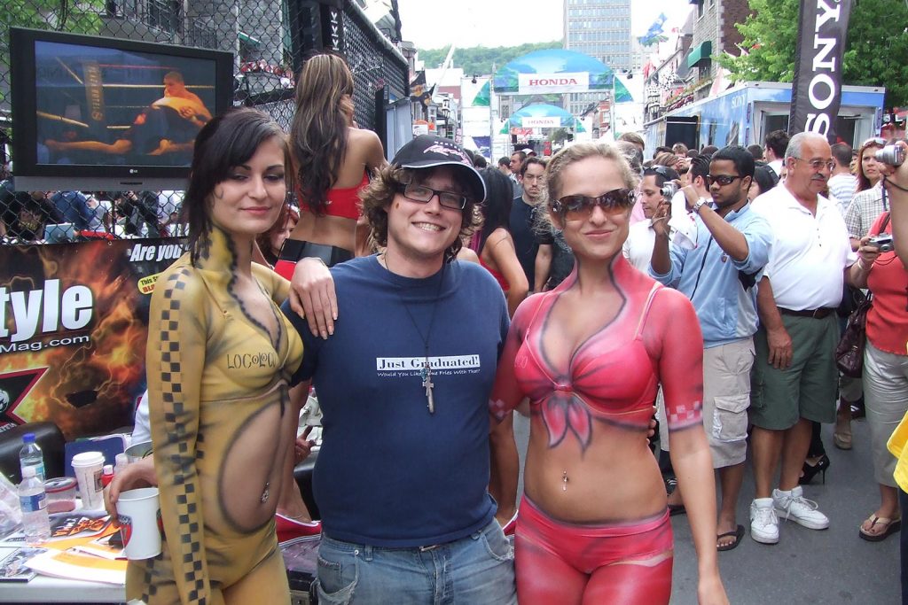 A guy between two girls in body paint with a crowd at the back in Montreal. F1 in Montreal