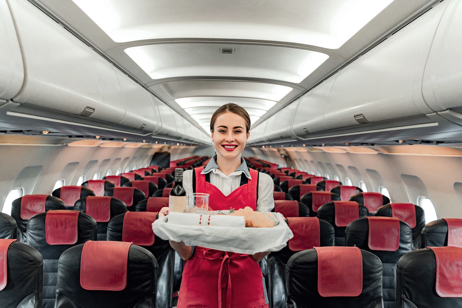 Flight stewardess holding tray of food and drink in passenger cabin of plane. How to survive long haul flights