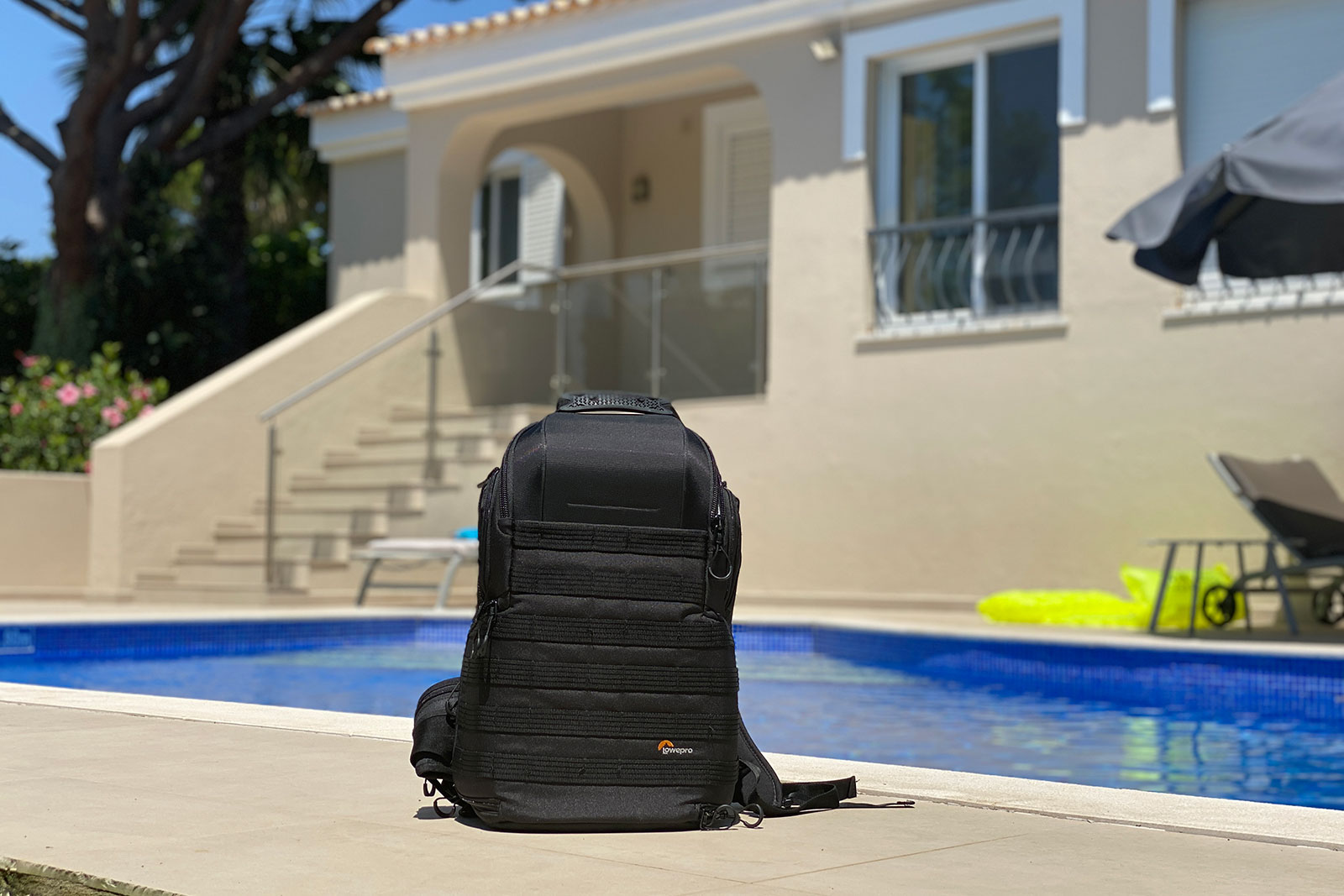 A small black backpack in front of a pool. The best backpack for travelling