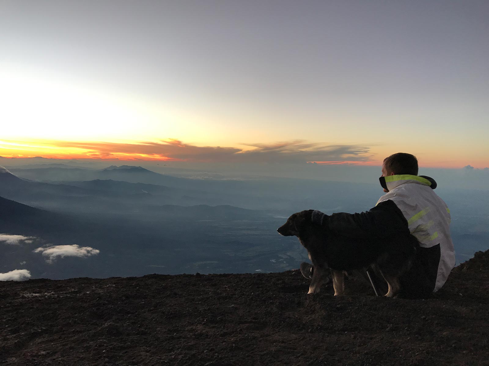 David Simpson and a friendly dog viewing sunrise above the clouds in Antigua, Guatemala. Volcano hiking in Guatemala
