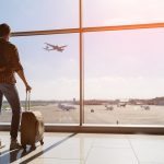 Man with a backpack and suitcase looking out of the airport window