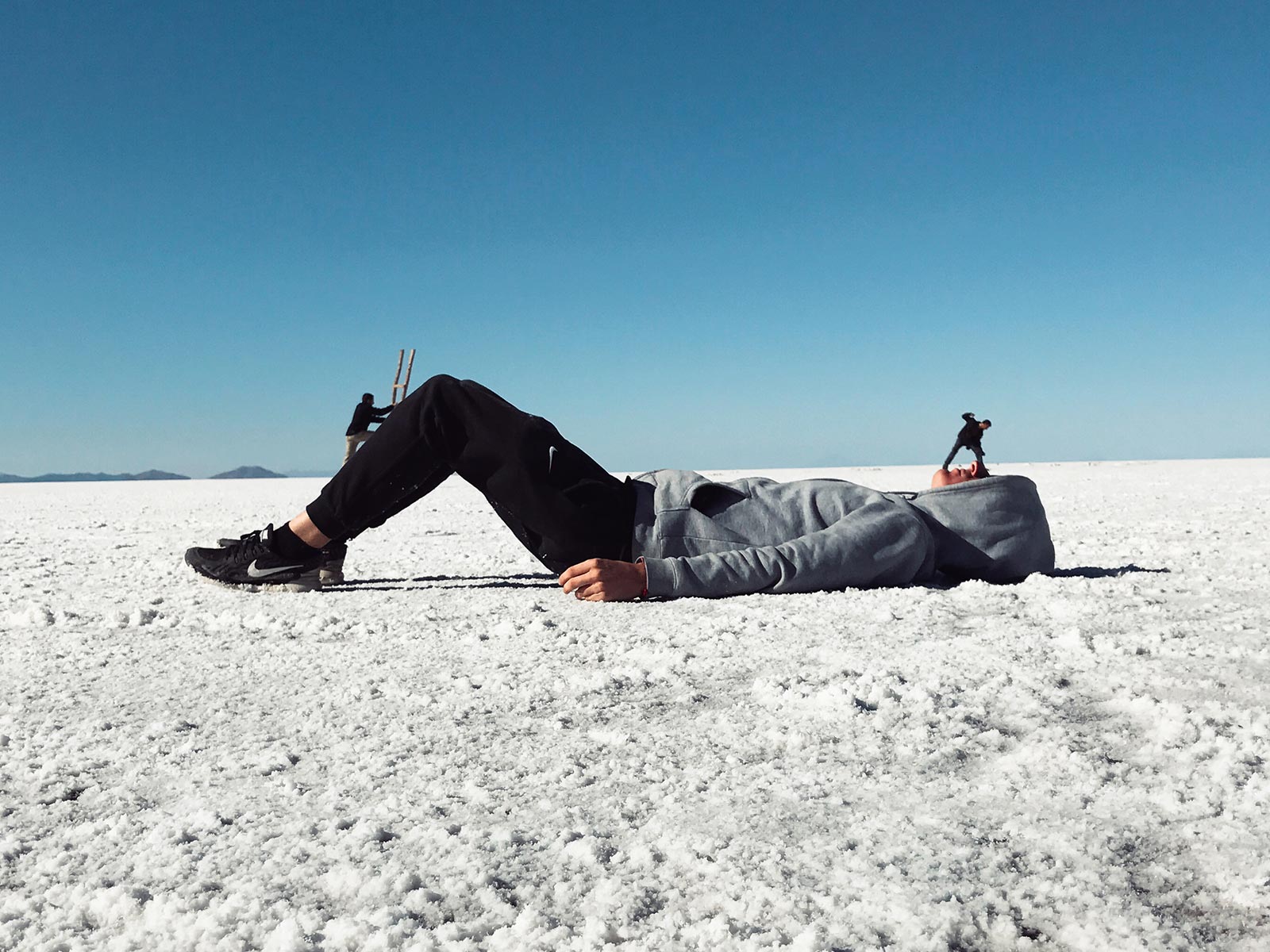 David Simpson lying down being climbed upon by two friends in Uyuni Salt Flat, Bolivia. Atacama desert & Bolivian salt flats road trip & full guide