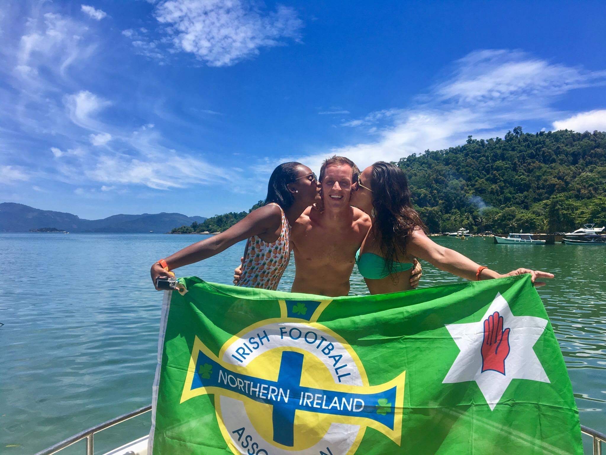 David Simpson being kissed by two friend girls while holding NI flag at speedboat tour in Ilha Grande, Brazil. Ilha Grande cures the hangover from hell