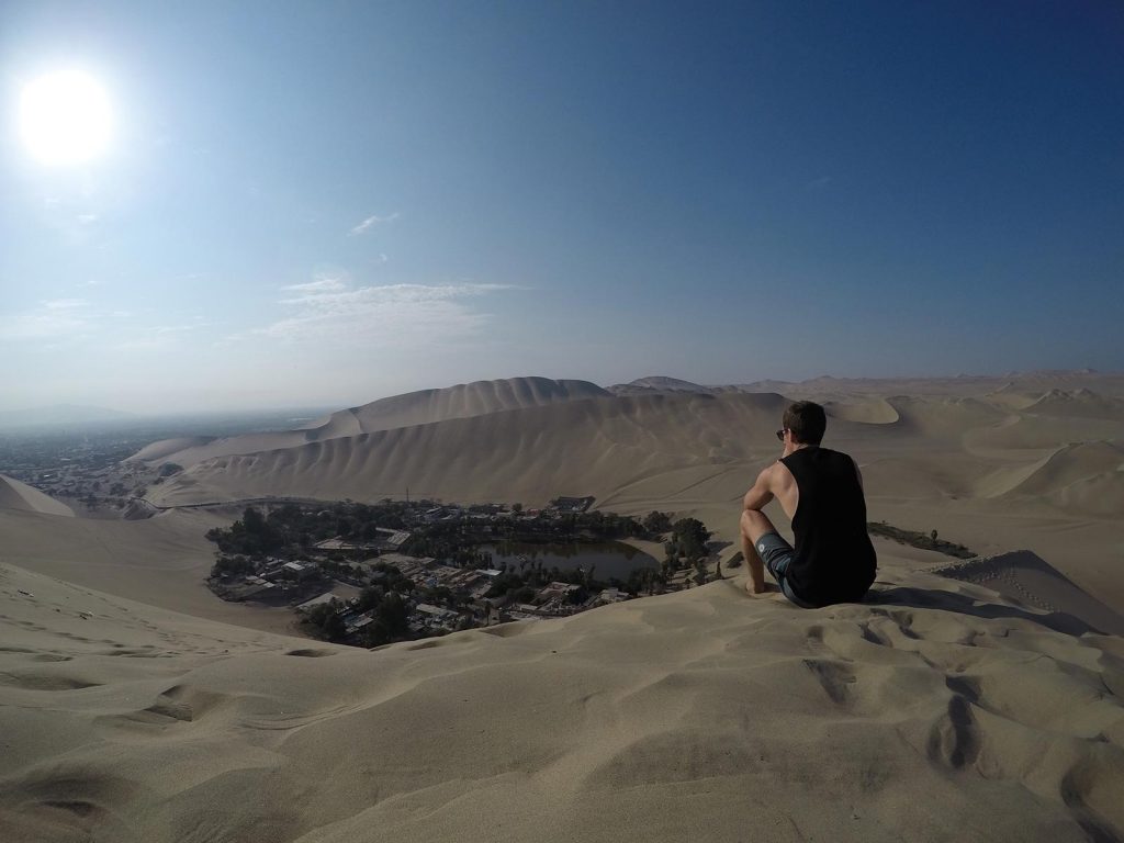 David Simpson sitting on a sand dune in Huacachina, Peru. Sand boarding in Huacachina & full guide