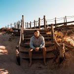 PORTRAIT IMAGE OF DAVID SIMPSON SITTING ON STEPS AT BEACH IN PORTUGAL