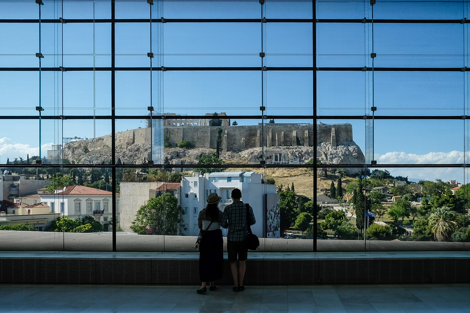 Couple viewing Acropolis thru a huge glass window. 10 things you must do in Athens