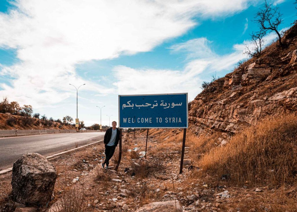 David Simpson standing by a bullet riddled Lebanon, Syria border sign. Where have I been so far