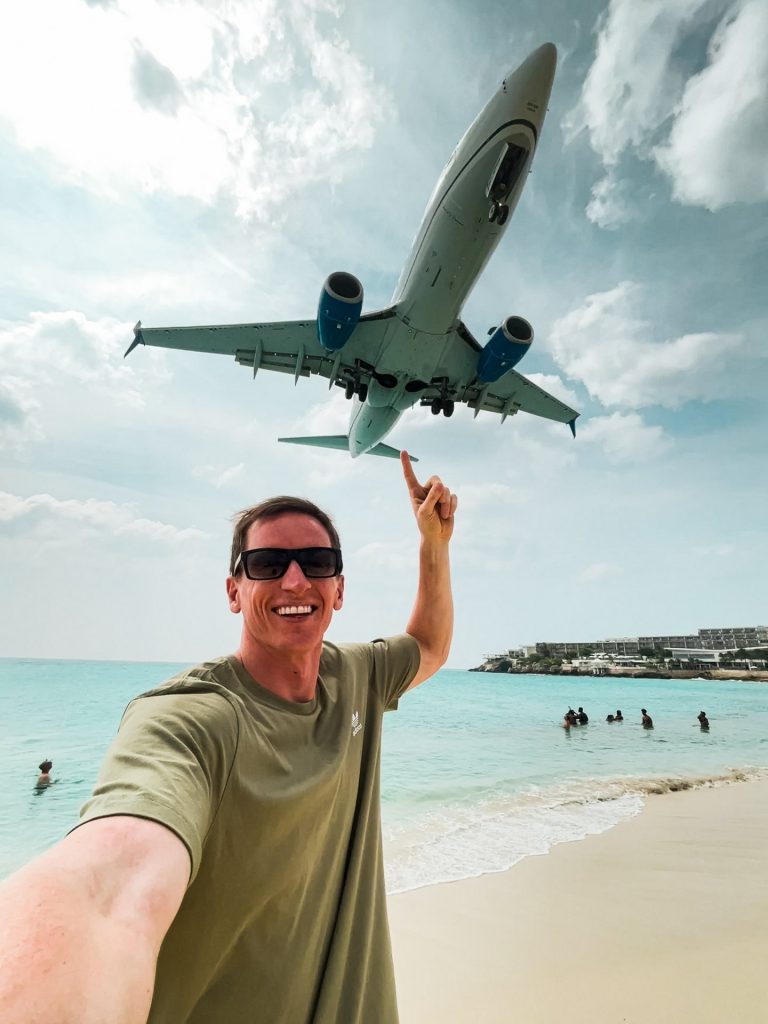 David Simpson standing by a beach with an plane flying overhead in Sint Maarten. Caribbean reflection; beaches, late PCRs & incredible accom