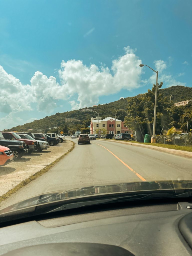 Road trip passing parked cars and view of a mountain in British Virgin Islands. BVI has me