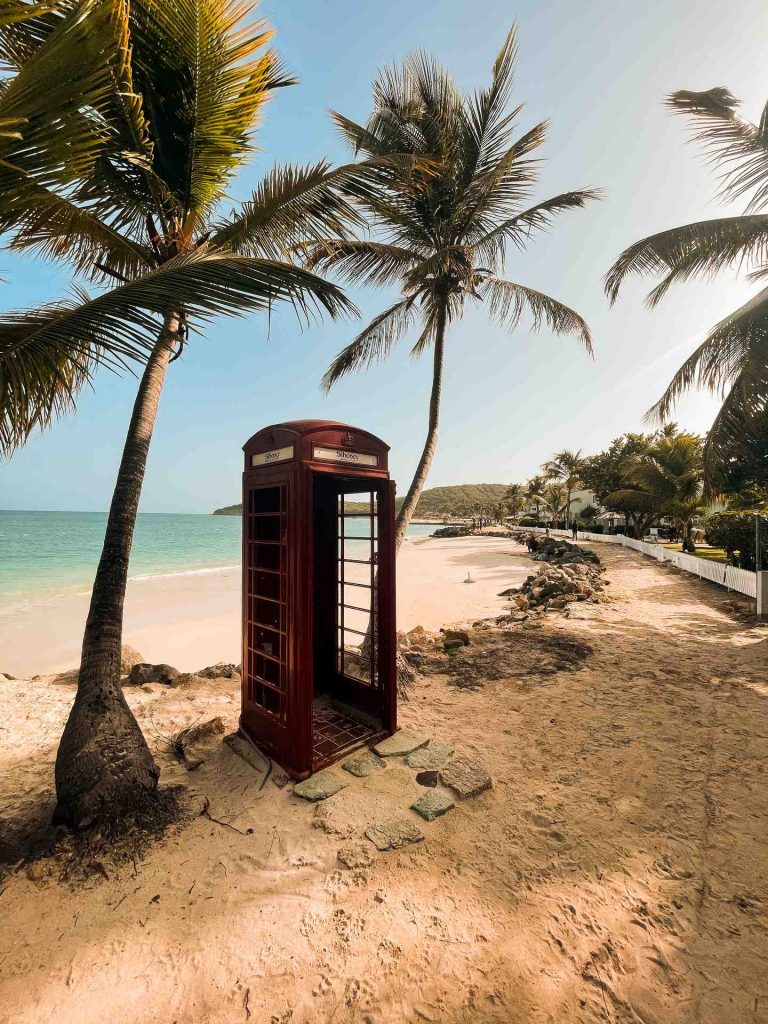 Red phone booth between trees at the beach in Antigua. Sir Vivian Richards & don’t hike in flip flops