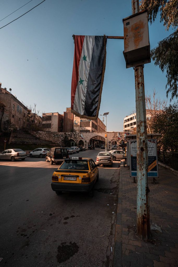 Flag hanging over a street with cars in Hama in Aleppo. A day in Hama, Syria