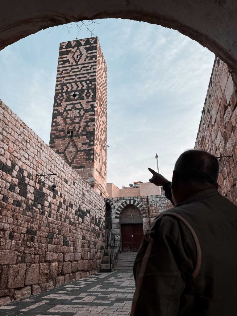 Man pointing at tower inside walls of mosque in Hama in Aleppo. A day in Hama, Syria