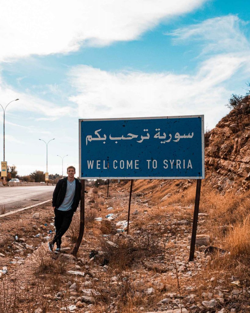 David Simpson arriving in Syria standing on welcome sign by the highway. The Syrian Series reflection post