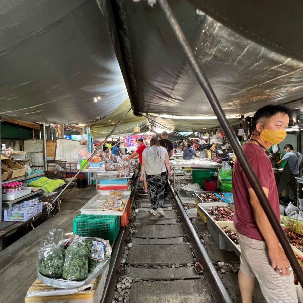 Market-goers and stalls at Maeklong train market in Thailand. Shotguns, markets and temples in Bangkok