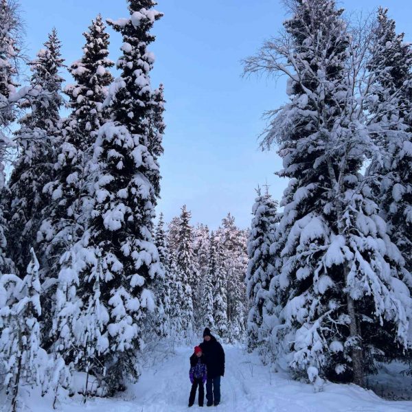 Dad and niece standing by the trees in the snow in Rovaniemi, Finland. Christmas Day in Lapland