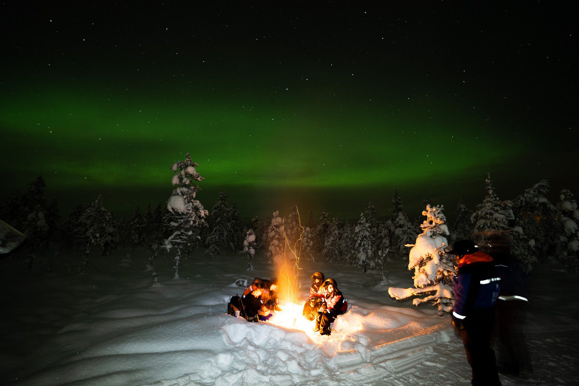 People by the fire on the snow at night in Rovaniemi, Finland. Christmas Day in Lapland