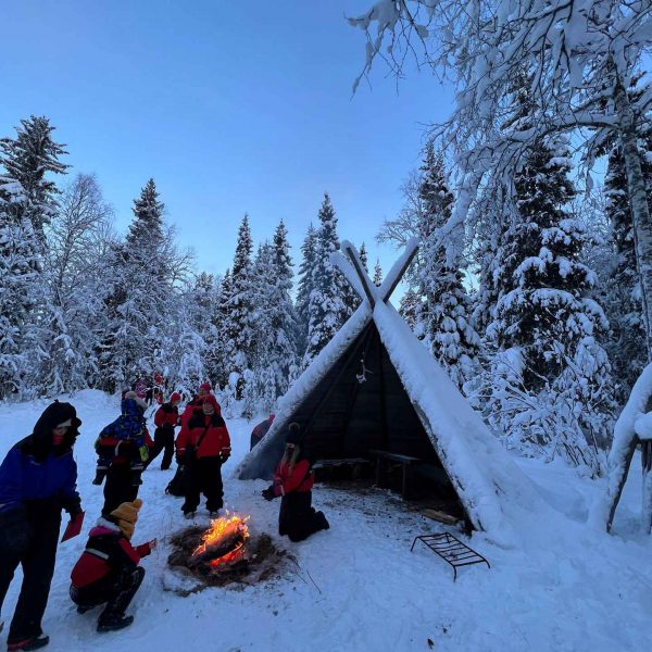 People outside a teepee by the snow covered woods in Rovaniemi, Finland. Christmas Day in Lapland