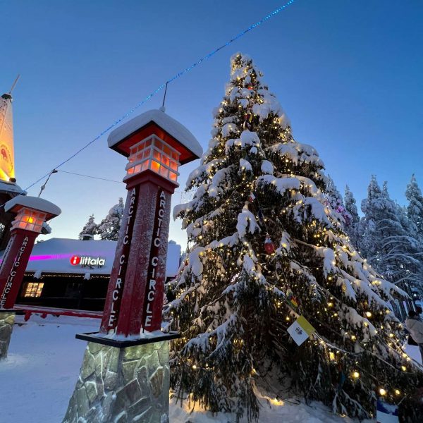 Arctic circle sign post by giant Christmas tree in Saariselka, Finland. Arriving in Santa Claus Village