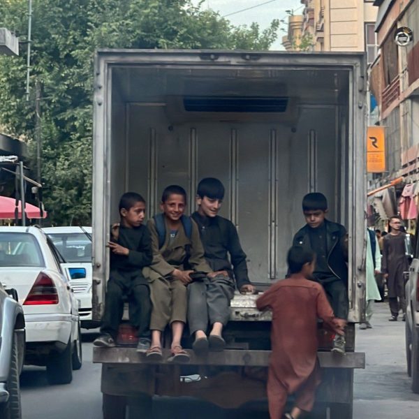 Local kids riding at the back of a van in Kabul, Afghanistan. Box camera and Afghan theme park
