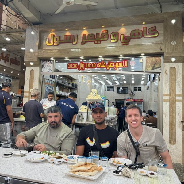 David Simpson and locals seated and eating in Iraq. A tour around Baghdad & the Al Anbar